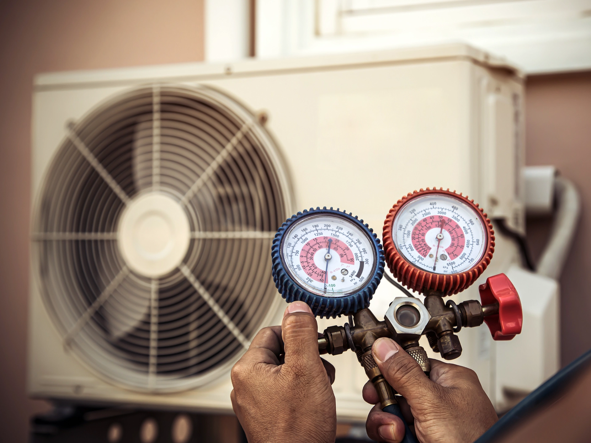 Man holding pressure gauges next to an air conditioning unit.
