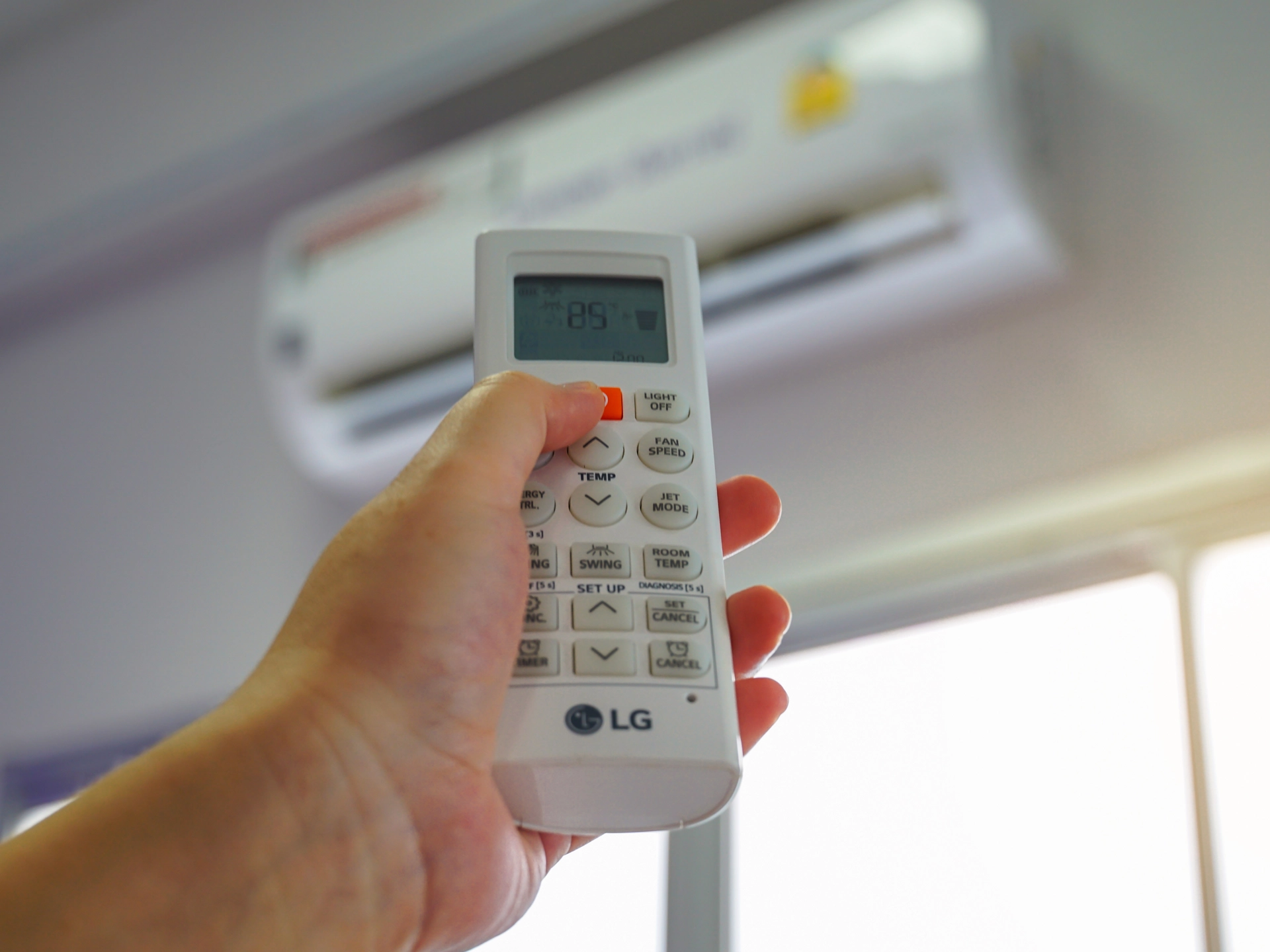 Hand holding an LG ductless HVAC remote control with display showing 85°F.