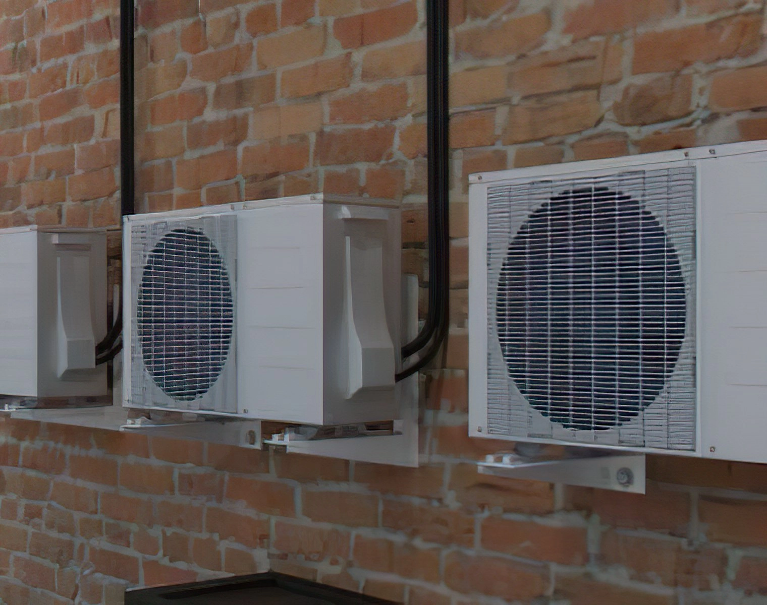 Three ductless mini split air conditioning units mounted on a brick wall.