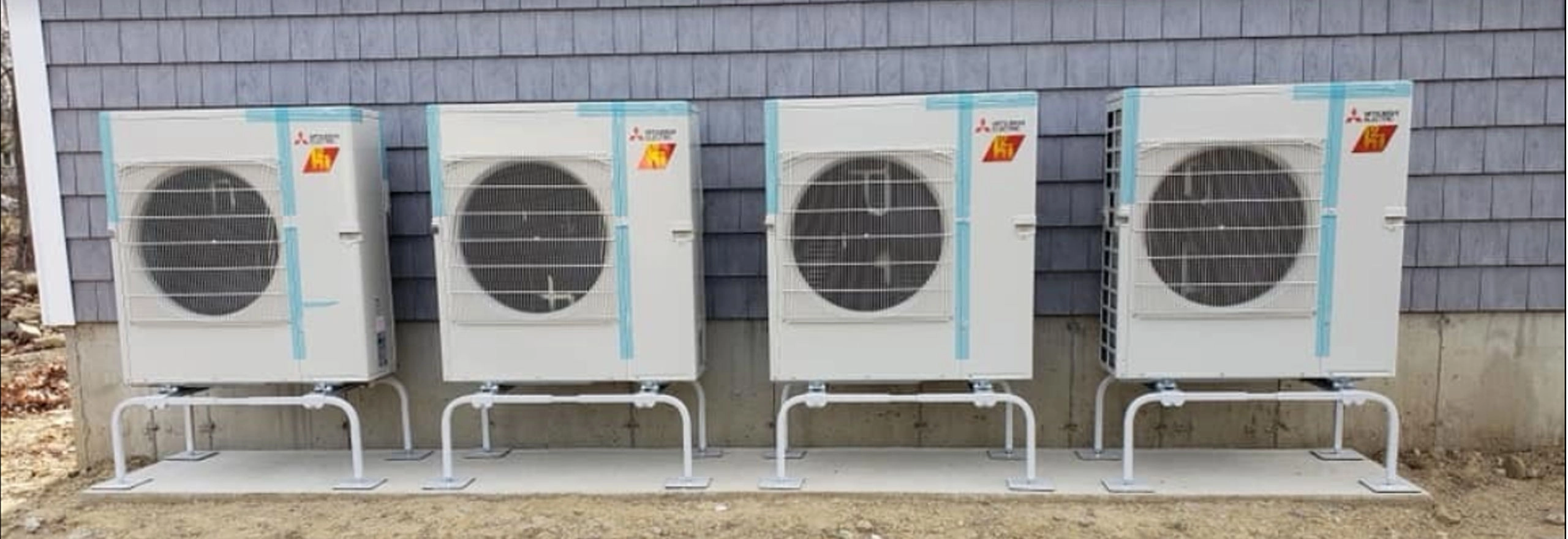 Four outdoor air conditioning units installed side by side on a concrete slab.