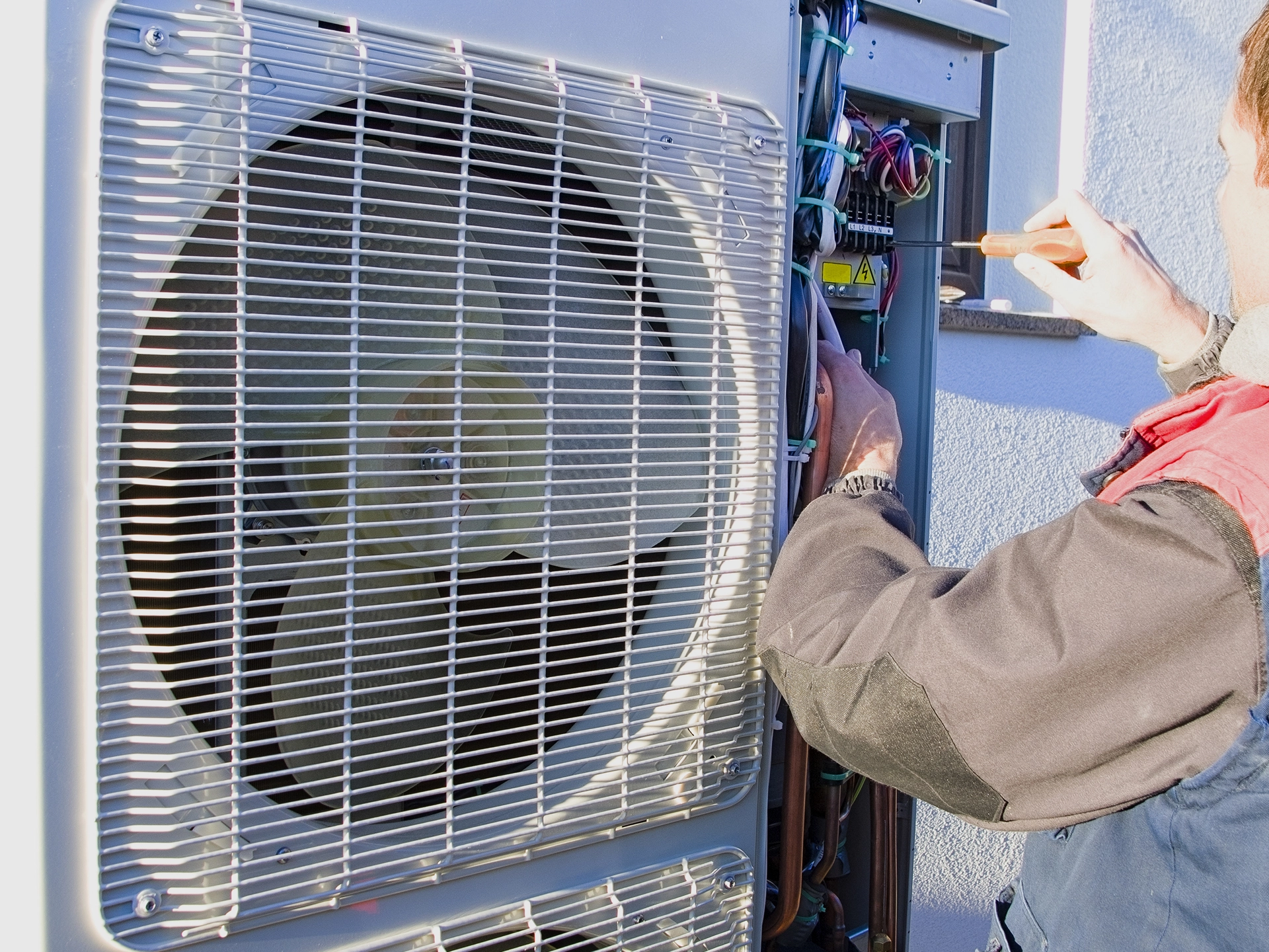 Technician servicing an outdoor air conditioning unit with a screwdriver.