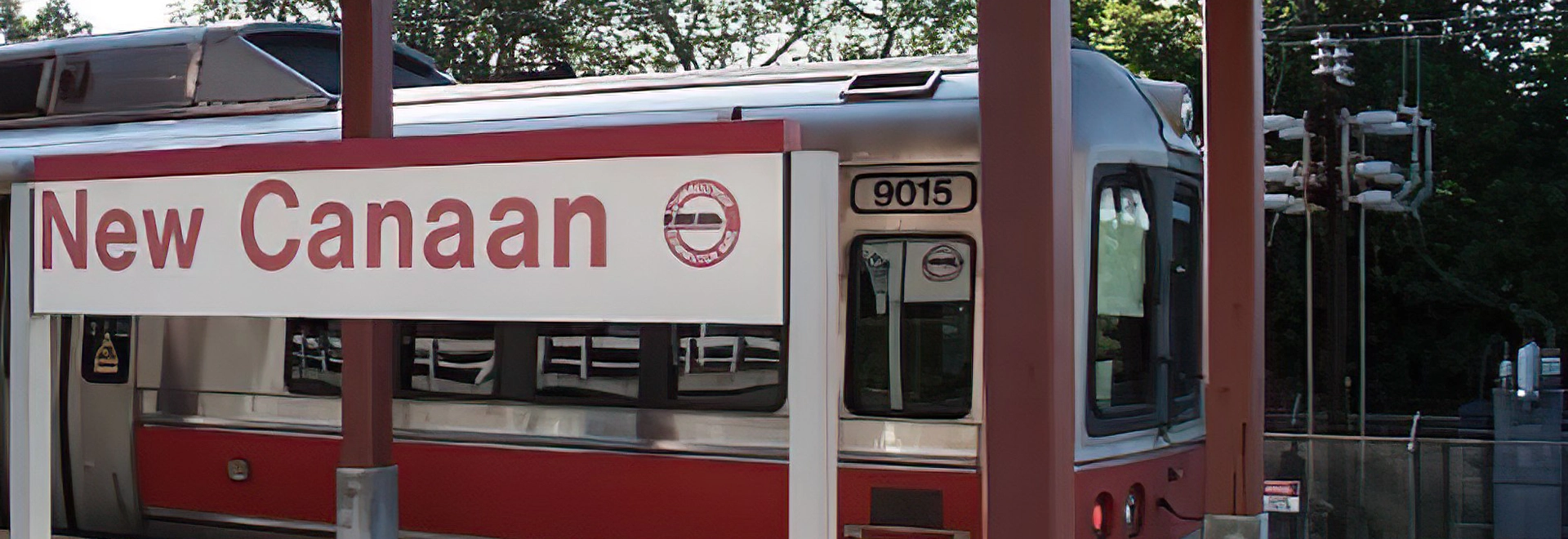 New Canaan Train Station sign with a train in the background.