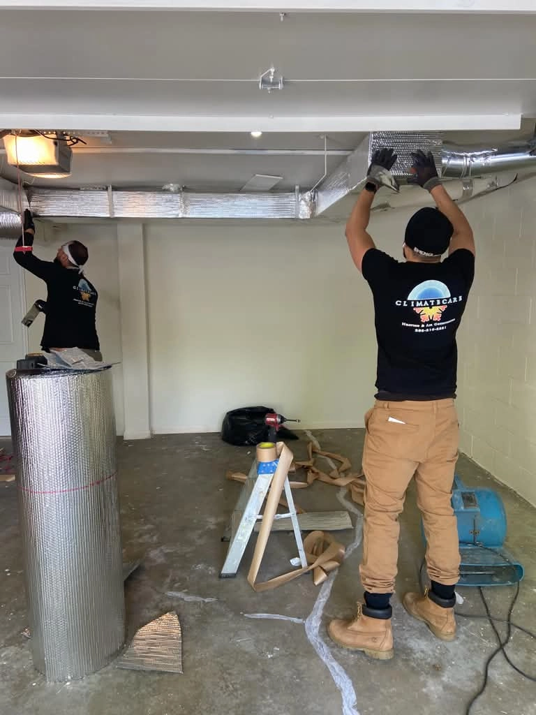 Two technicians installing HVAC ductwork in a basement.