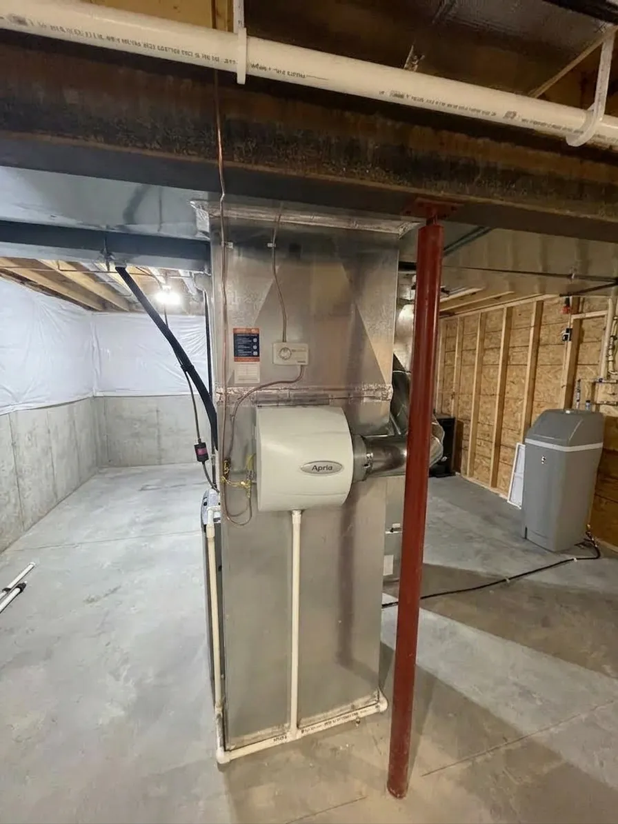 Air handling unit in a basement with exposed ductwork and concrete flooring.
